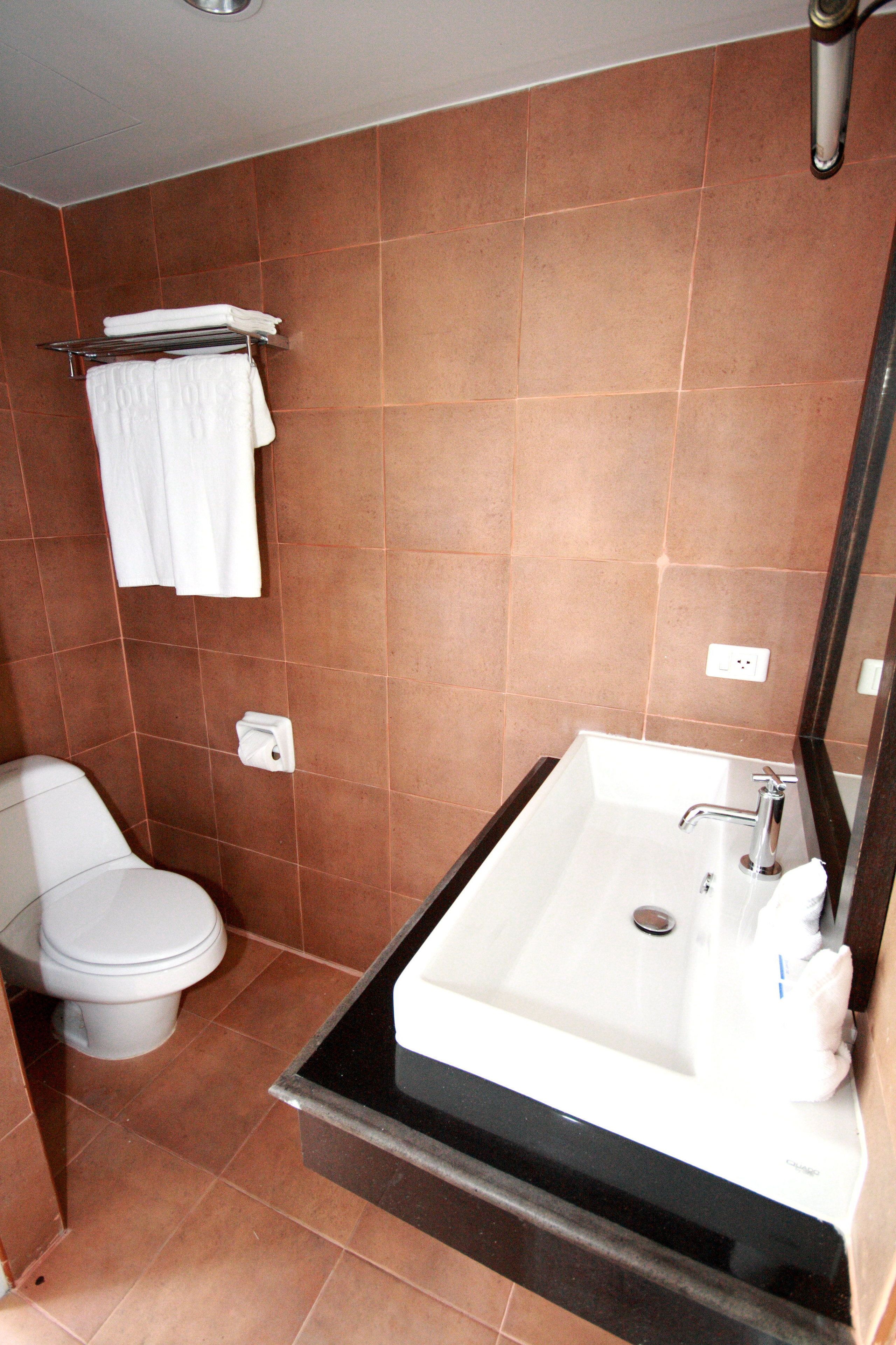 A bathroom with a white toilet, a sink with a mirror, and brown tiled walls.