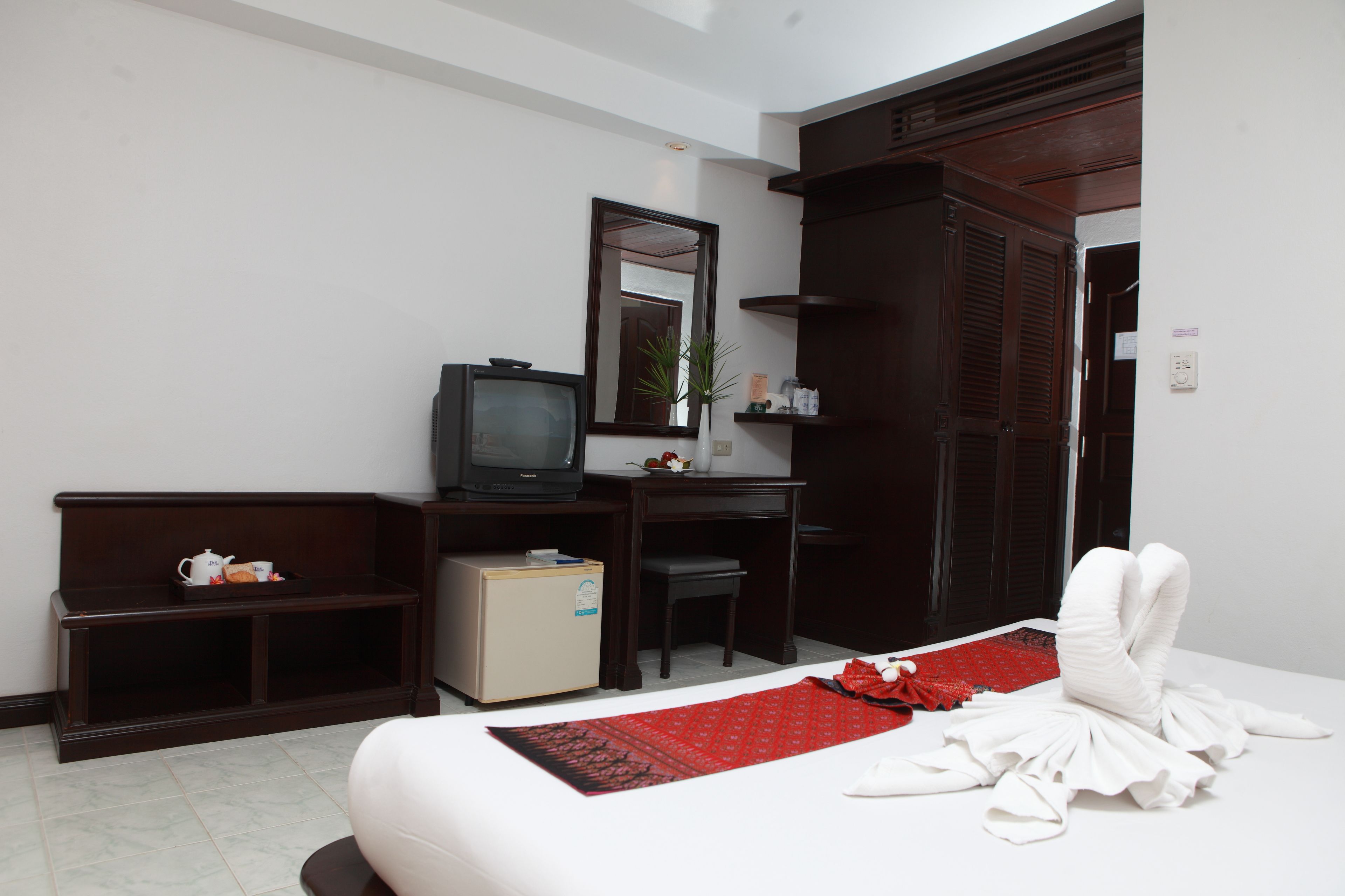 A hotel room with a bed, a desk, a television, a small refrigerator, and a mirror.