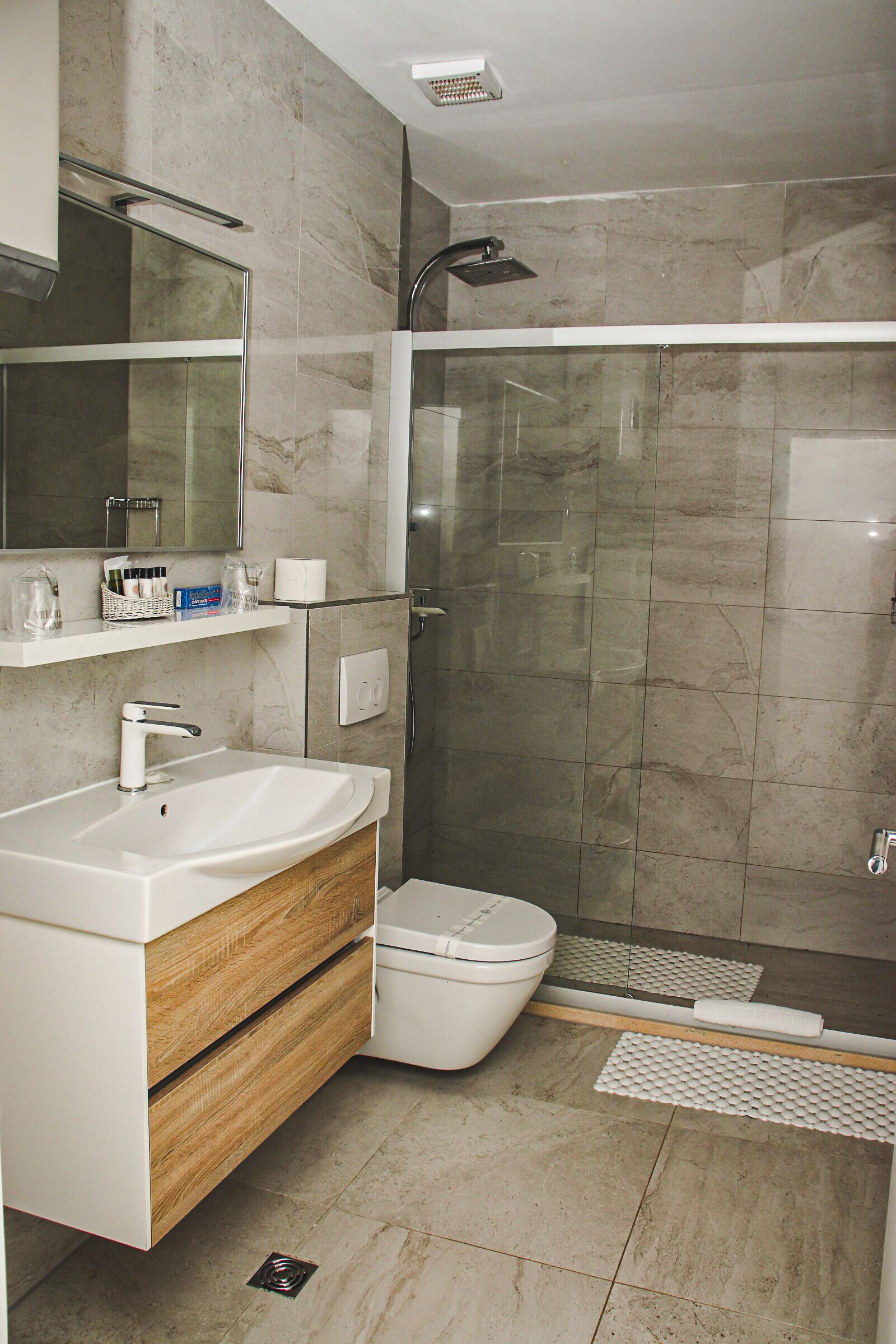 Une salle de bain moderne avec une douche à parois de verre, un lavabo blanc et un meuble-lavabo en bois.