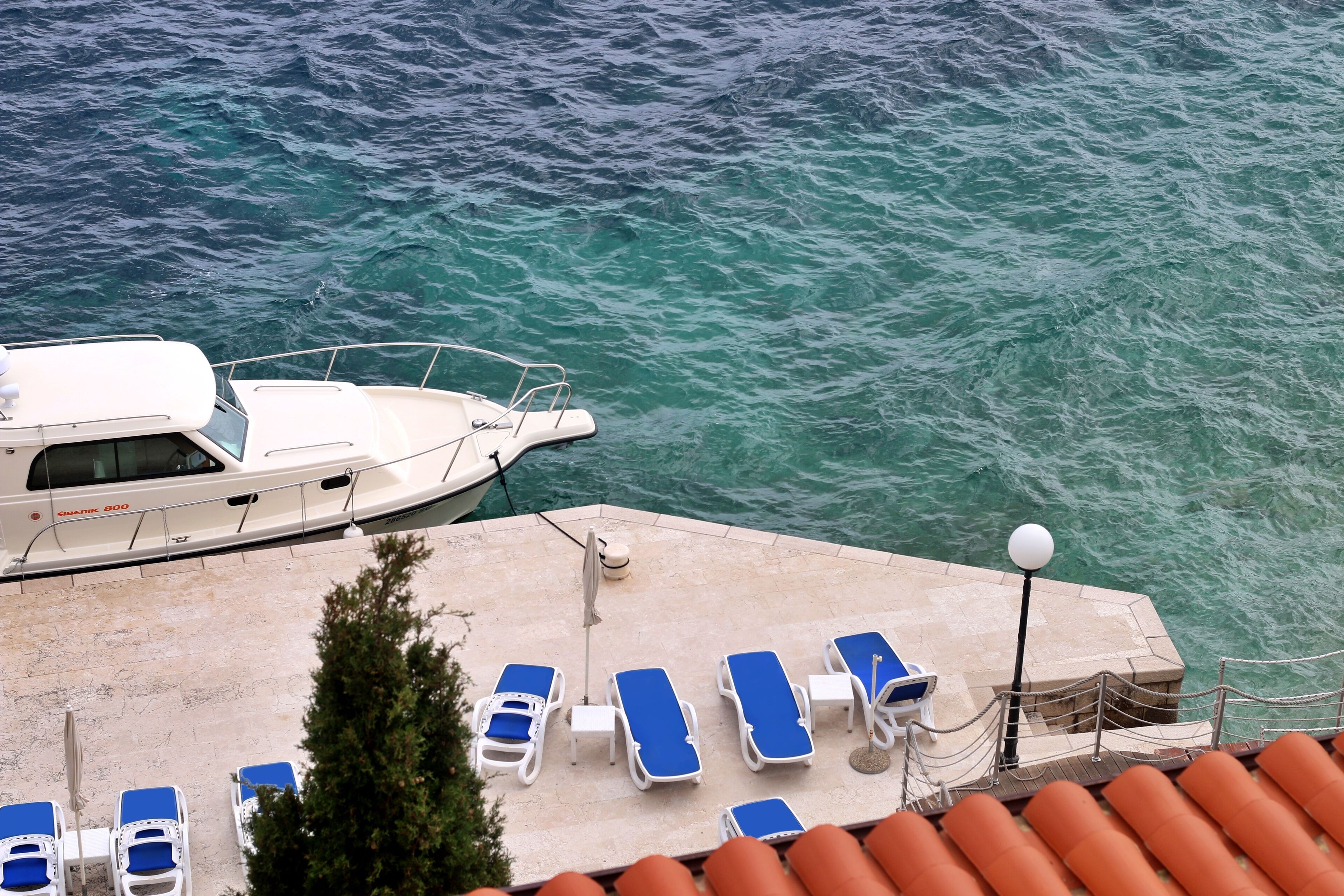 A yacht docked at a marina with lounge chairs and a lamp post.