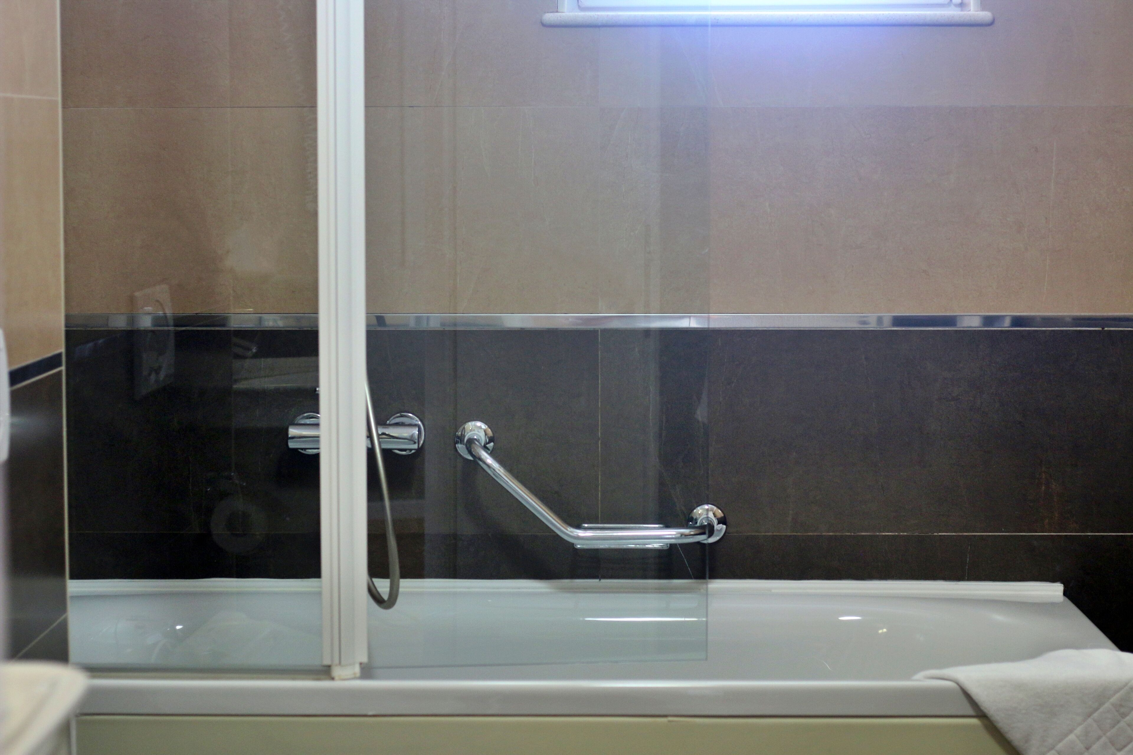 Un baño moderno con ducha de vidrio, barra de apoyo y bañera blanca.