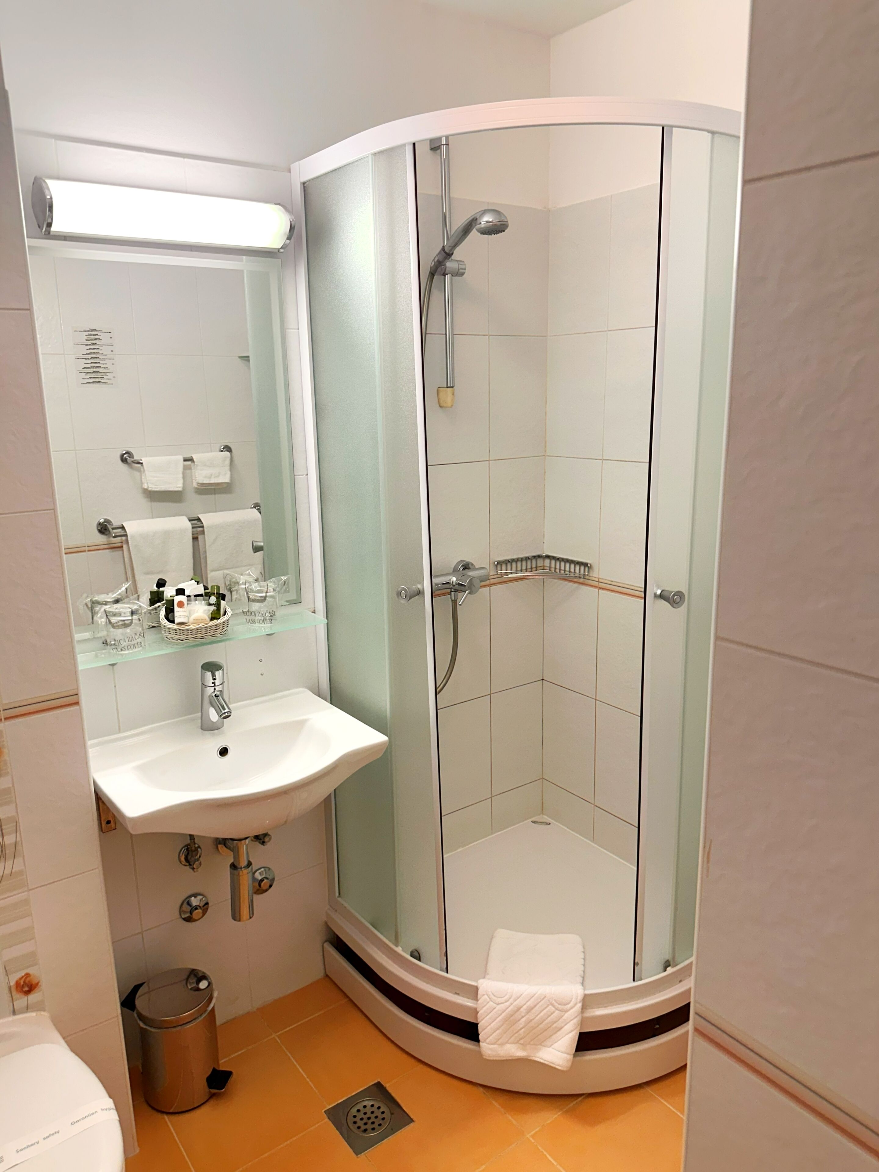 Un baño moderno con ducha envuelta en vidrio, un lavamanos con espejo y un cubo de basura.