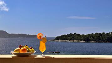 A balcony with a fruit bowl and a drink, overlooking a body of water and a distant shoreline.