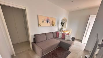 Una sala moderna con un sofá seccional gris, un tapete marrón, un televisor de pantalla plana y una zona de comedor con una mesa y sillas.