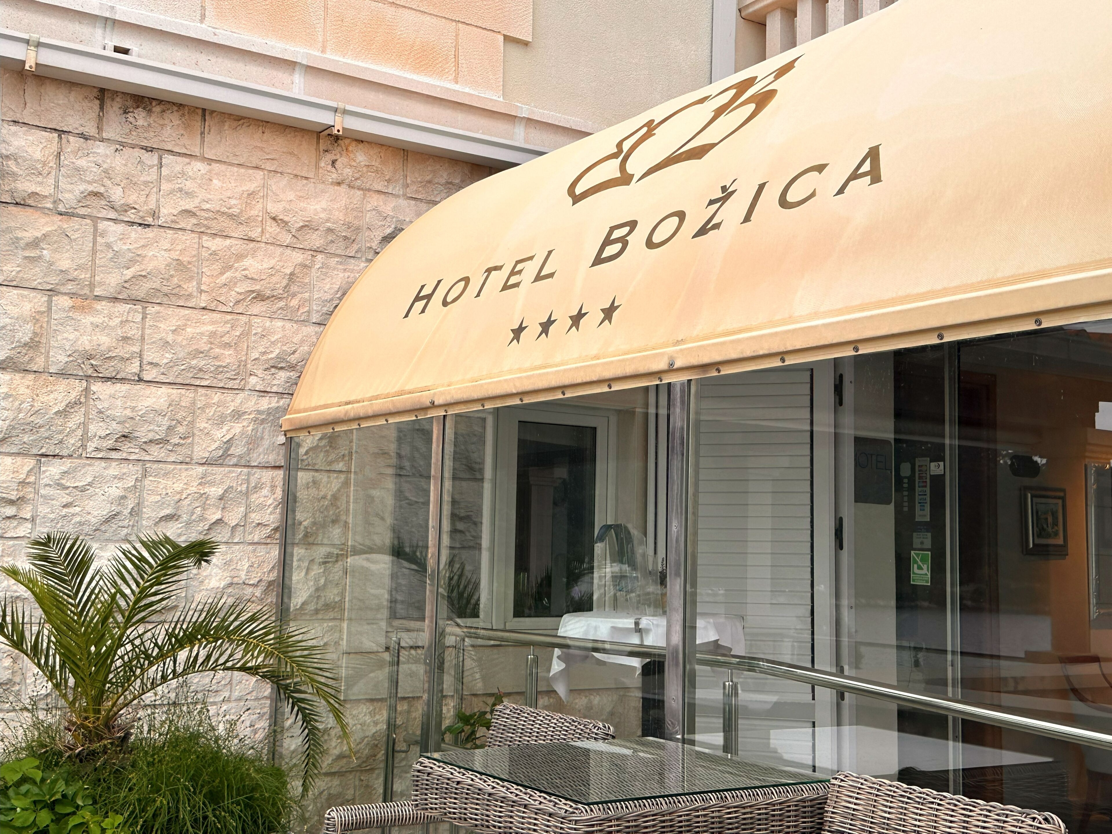 A hotel entrance with a stone facade, a covered outdoor seating area, and a sign reading "HOTEL BOŽICA".