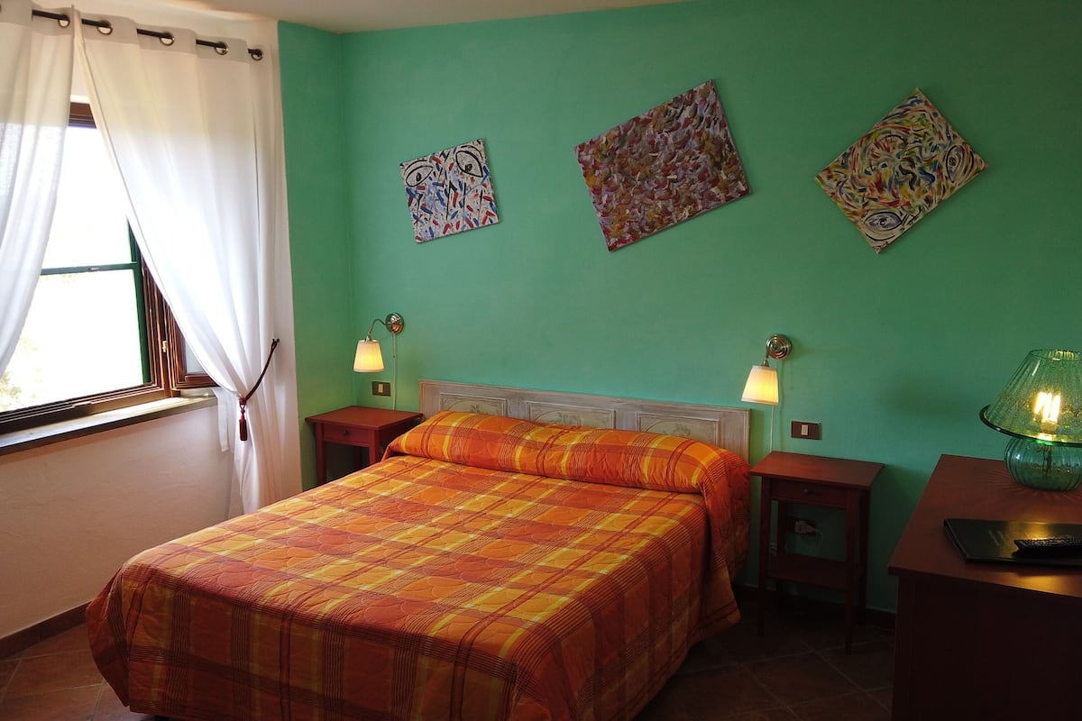 A bedroom with a bed, two bedside tables, a lamp, and three paintings on the wall.