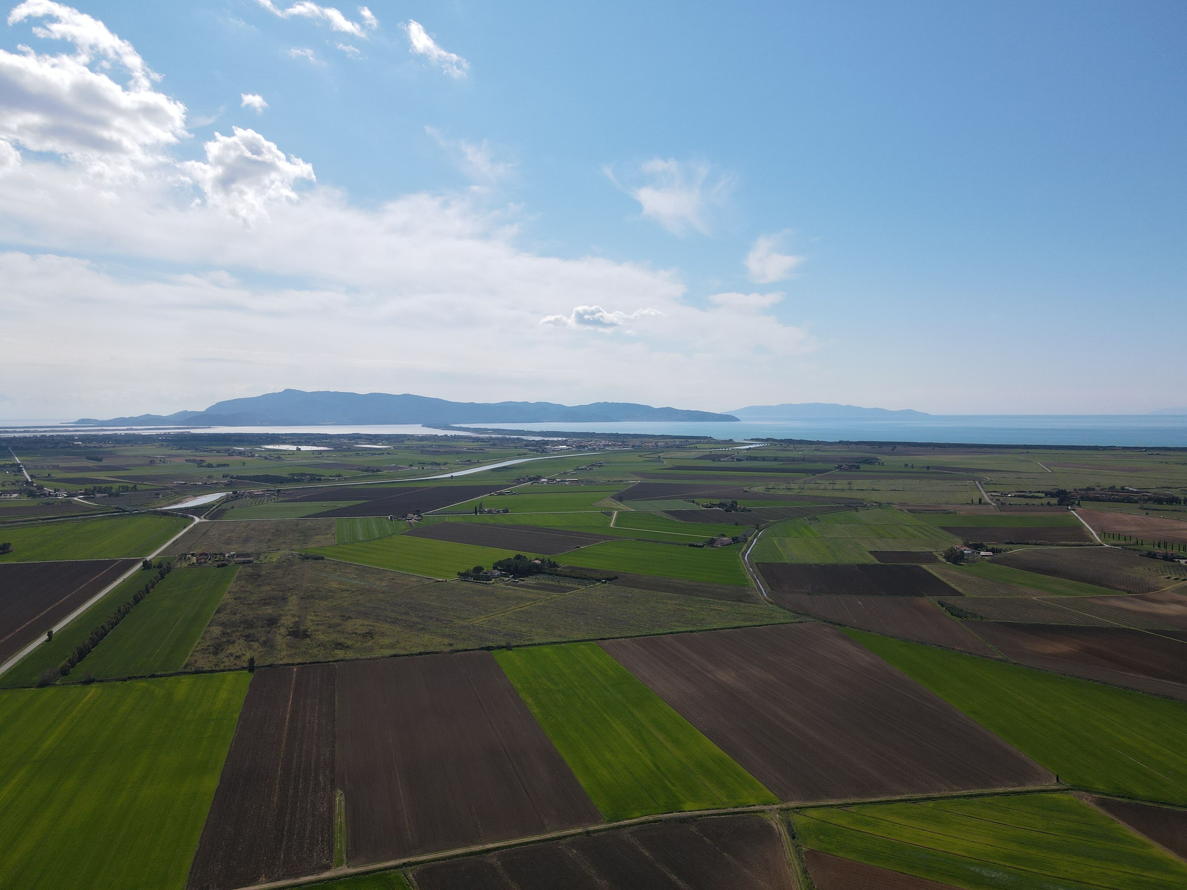 Een vogelperspectief van een landelijk landschap met velden, een weg en verafgelegen bergen.