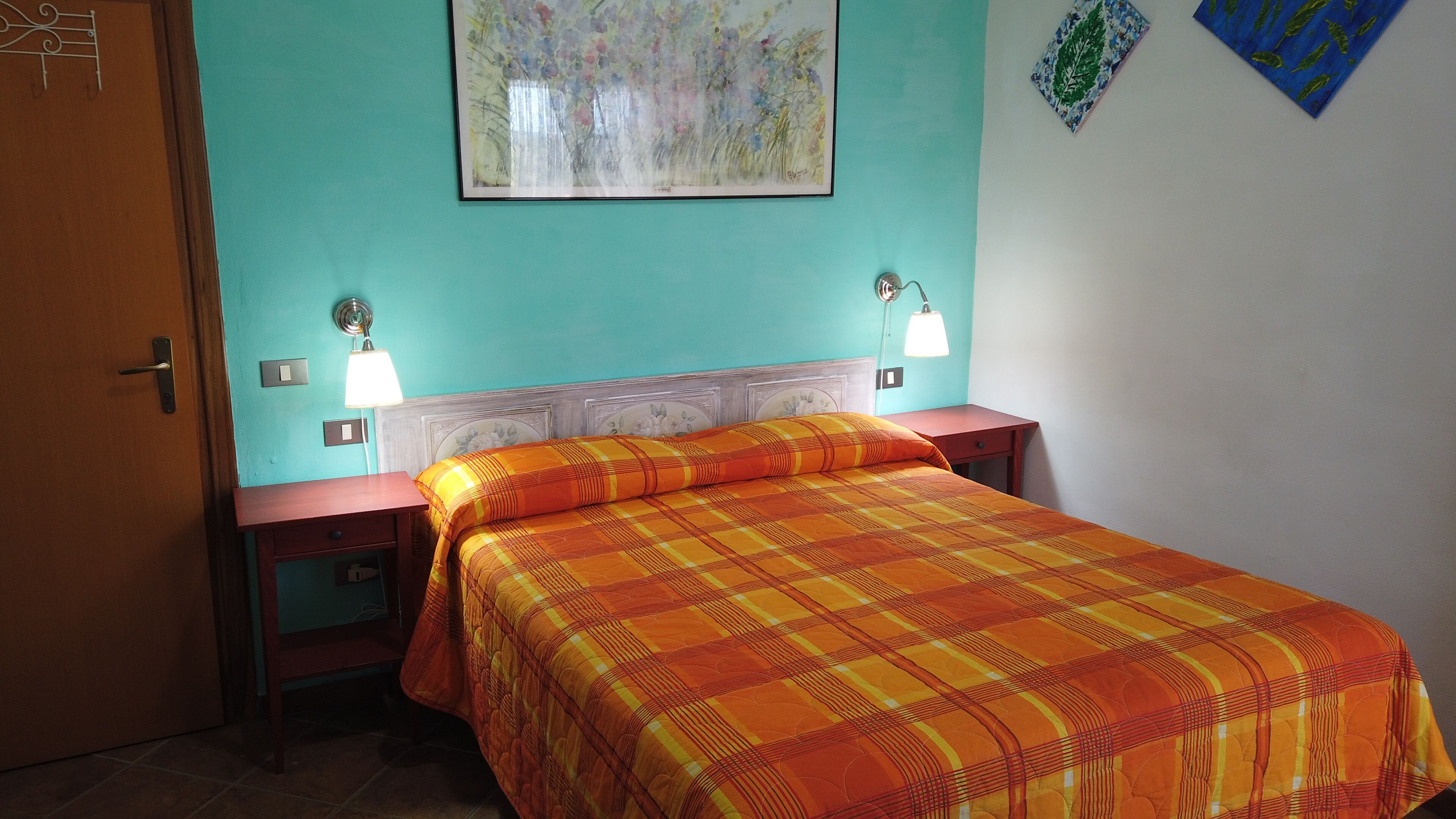 Una habitación con una cama, dos mesitas de noche, una lámpara de pared y una puerta.