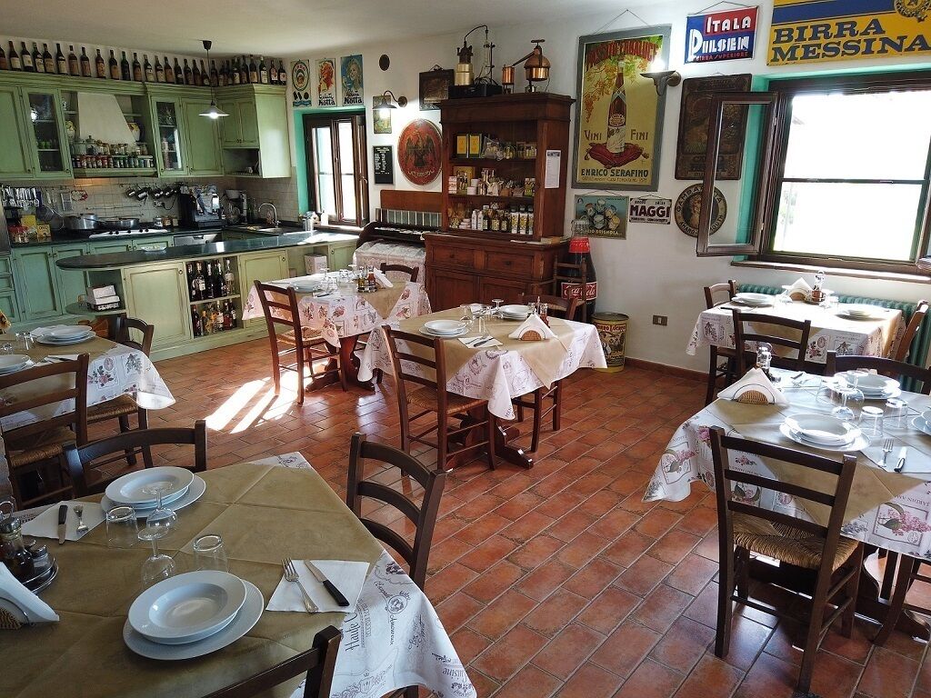 Un restaurante con varias mesas dispuestas para los comensales, una zona de cocina con armarios verdes y diversos alimentos y bebidas exhibidos.