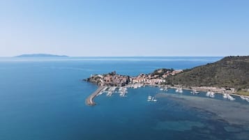 Vista aérea de un pueblo costero con un puerto deportivo, edificios y un paisaje montañoso.