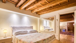 A bedroom with a wooden ceiling, a large bed with floral bedding, a nightstand with a lamp, and a mirror reflecting the room. - Boutique Hotel Scalzi - Adults Only (Verona)