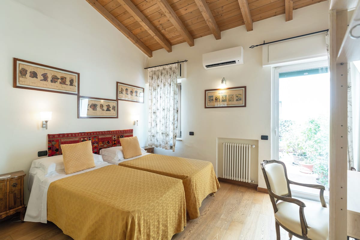 A bedroom with two beds, a wooden ceiling, a radiator, and a window with a view.