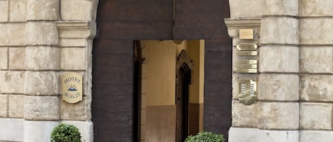 Un edificio de piedra con una entrada arqueada, una placa con el número 5 y dos macetas con plantas en la acera.