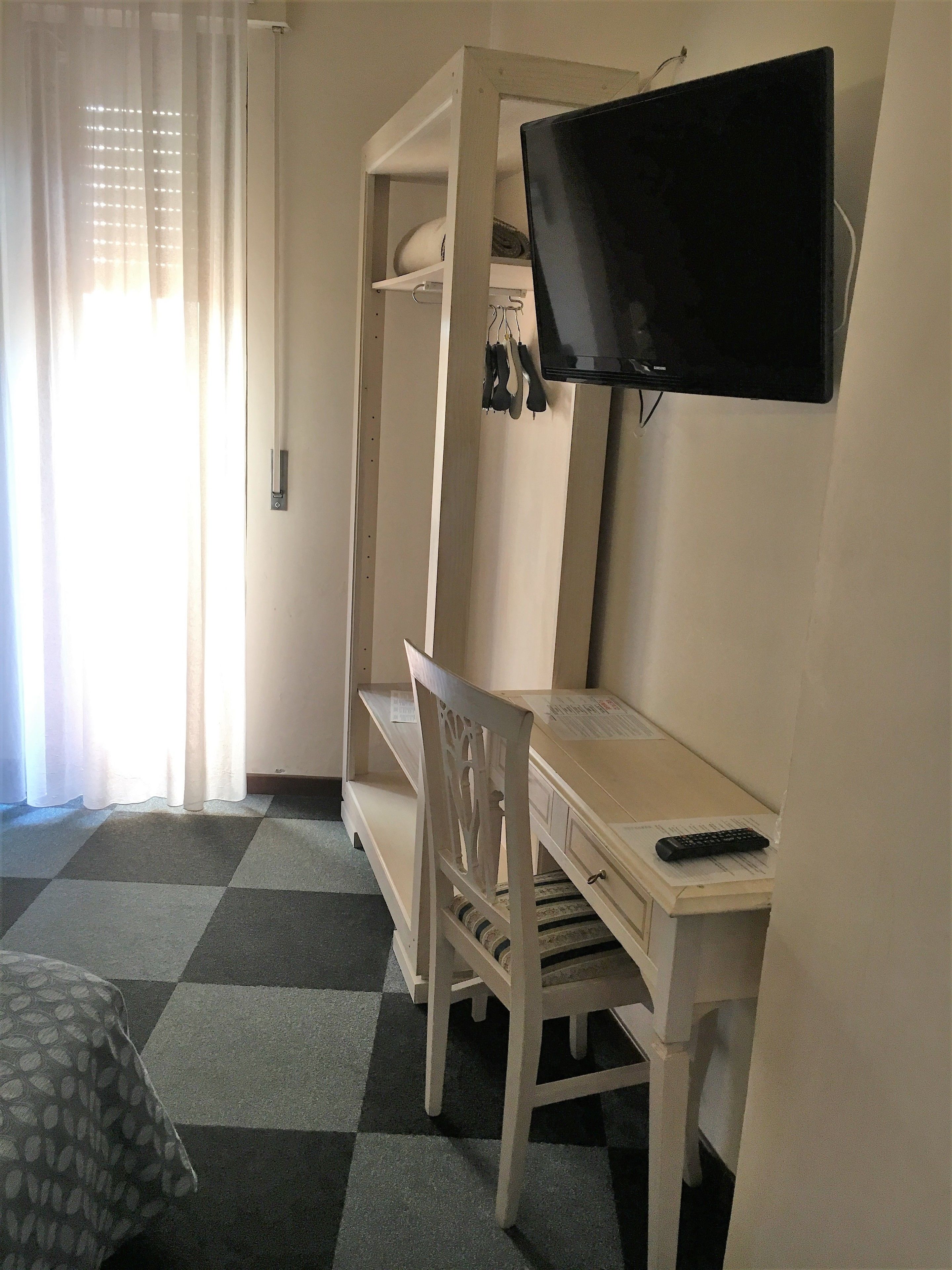 A room with a bed, a desk with a chair, a television mounted on the wall, and a window with curtains.
