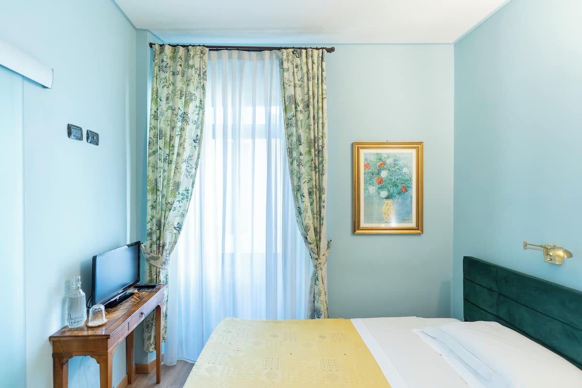 A bedroom with a bed, a bedside table with a television, and a painting on the wall.