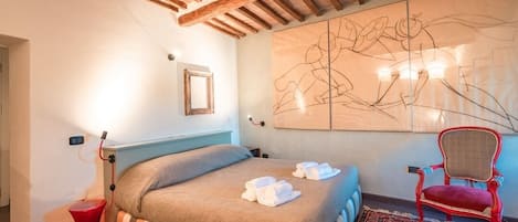 A hotel room with a bed, a red chair, a large abstract painting, and a wooden ceiling.