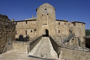 A historic stone building with a central tower, a staircase leading up to the entrance, and a paved pathway.