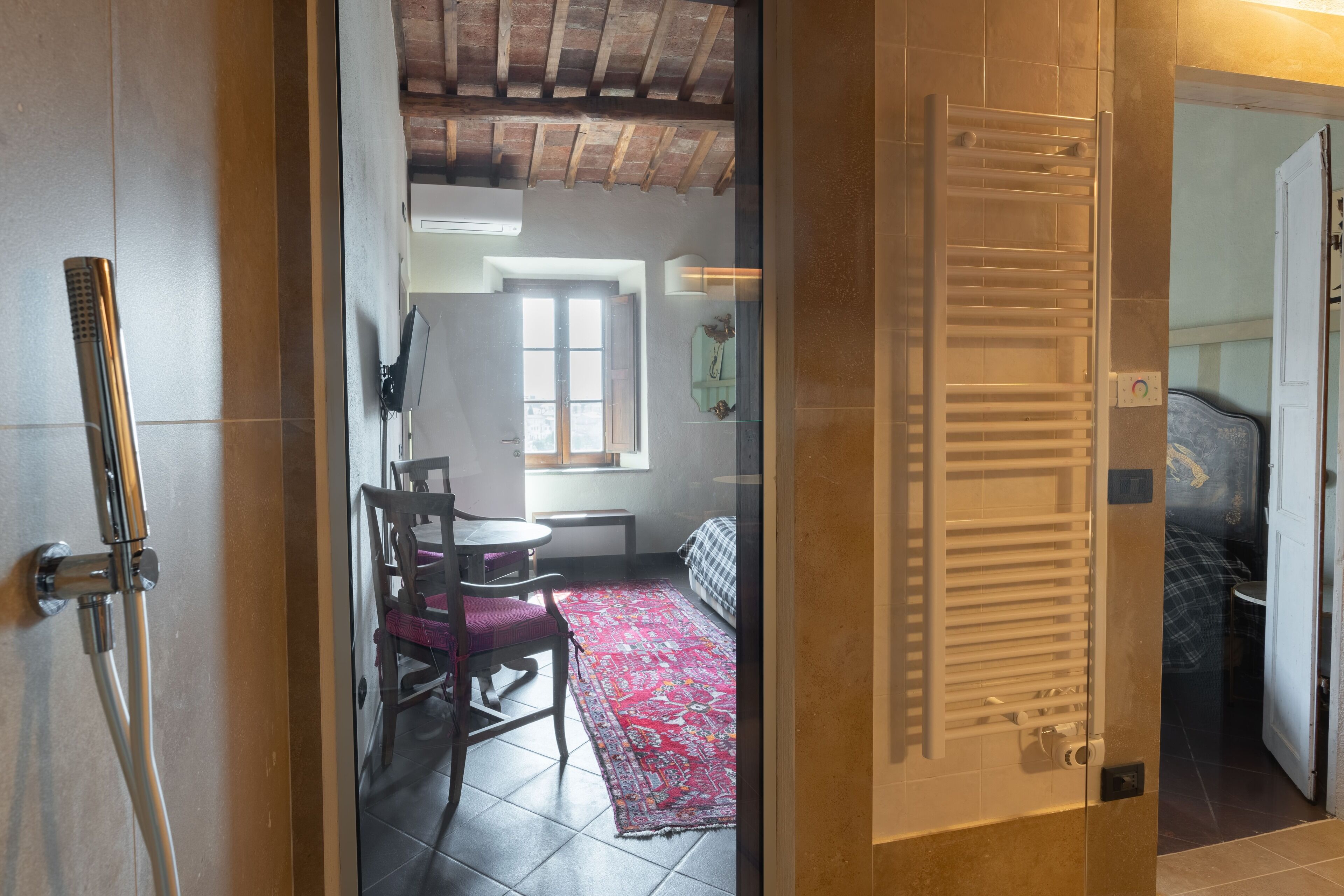 Una stanza con una porta in vetro che dà su un'area pranzo con tavolo e sedie, un tappeto rosso decorato e una finestra con luce naturale.