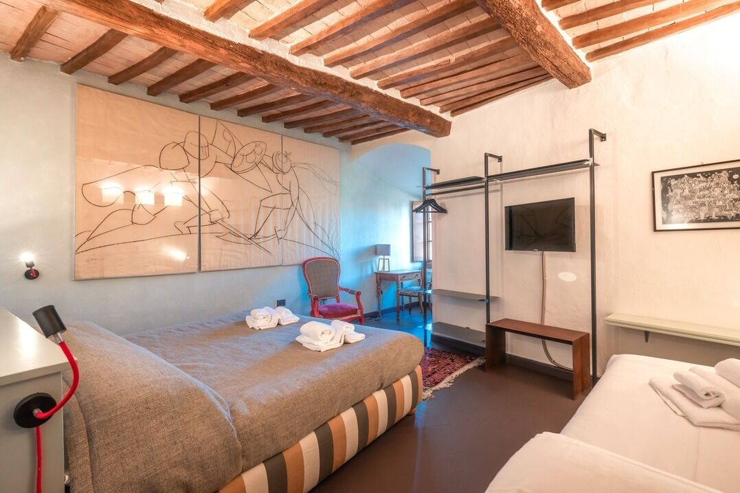 Une chambre d’hôtel avec un lit, une banquette, une chaise, un téléviseur et un grand tableau abstrait accroché au mur.
