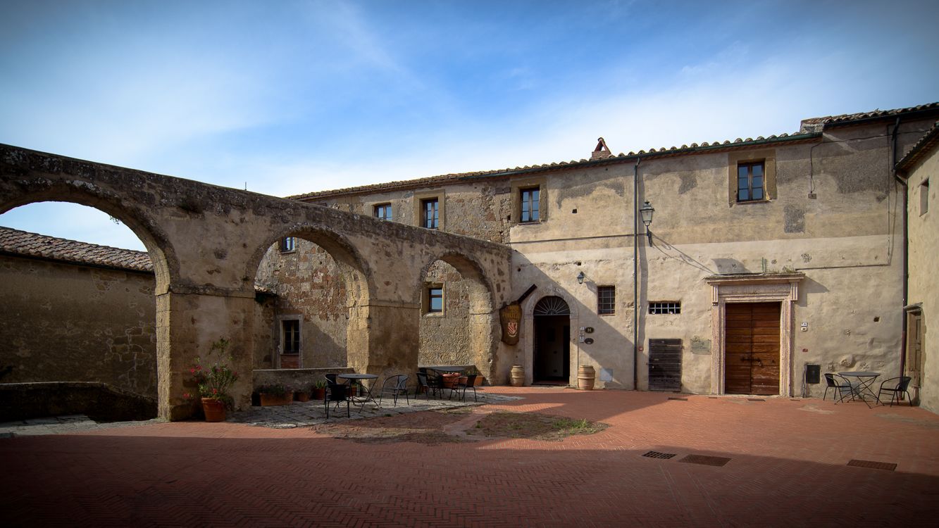 Un patio exterior con arcos de piedra, un camino de ladrillo y un edificio con tejado de tejas.