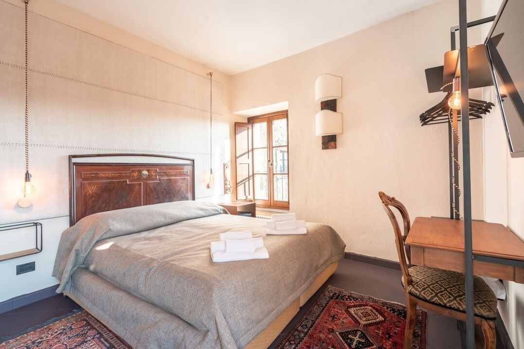 A hotel room with a large bed, a wooden headboard, a desk with a chair, a hanging light fixture, and a window with a view.