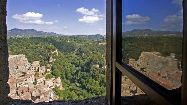 A view from a window overlooking a historic town with terraced buildings and a mountainous backdrop. - Hotel della Fortezza (Sorano)