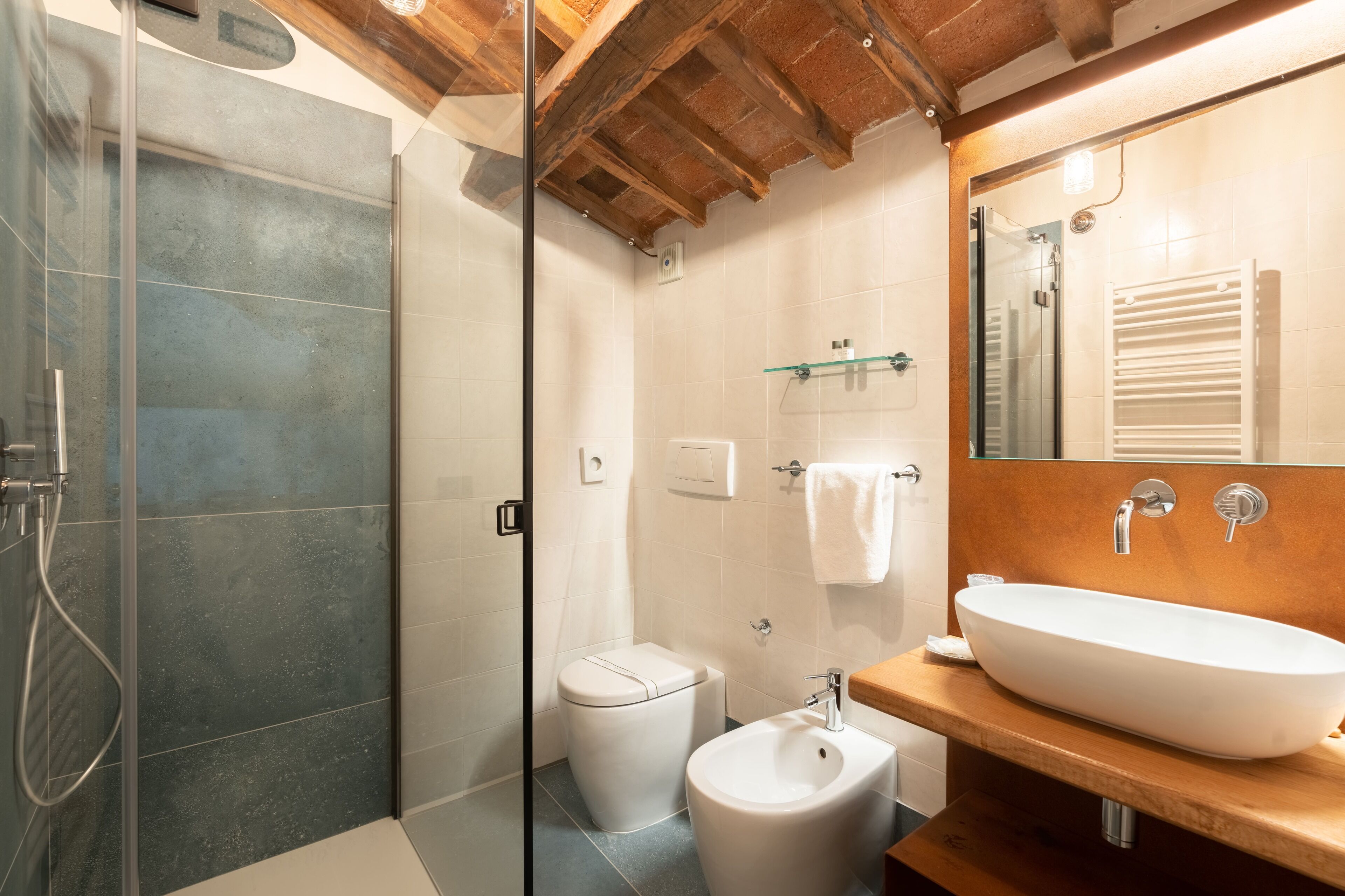 A modern bathroom with a glass-enclosed shower, a white toilet, a bidet, and a wooden vanity with a large sink.