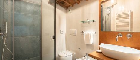 A modern bathroom with a glass-enclosed shower, a white toilet, a bidet, and a wooden vanity with a large sink.