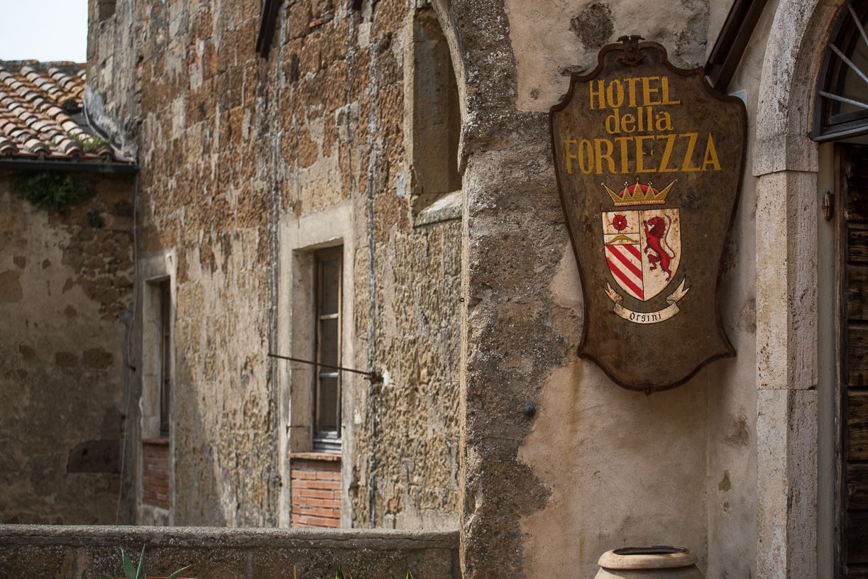 Un edificio de piedra desgastado por el tiempo con un letrero que dice “HOTEL della Fortezza” y un escudo de armas.