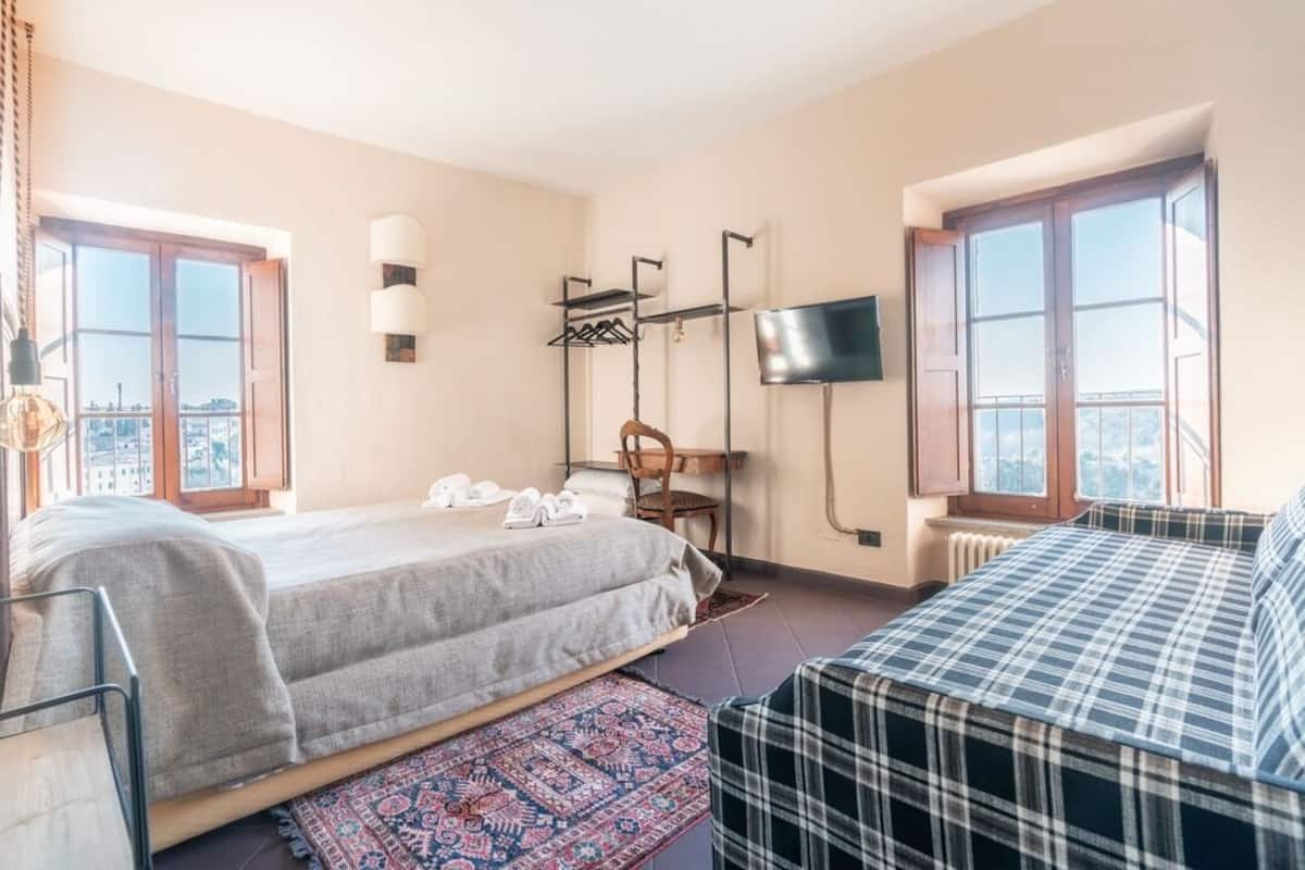 A bedroom with a bed, a chair, a TV, and a window.