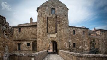 Un edificio storico in pietra con una torre centrale, un ingresso ad arco e un cortile interno.