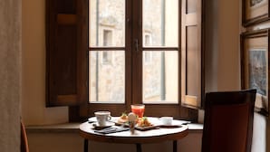 A dining table with a meal, a drink, and a chair in a room with a large window and a painting on the wall. - Hotel della Fortezza (Sorano)