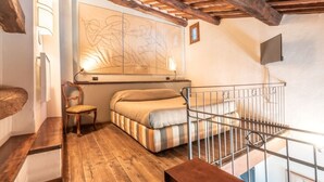 A cozy room with a wooden floor, a bed with striped bedding, a chair, and a large abstract painting on the wall. - Hotel della Fortezza (Sorano)