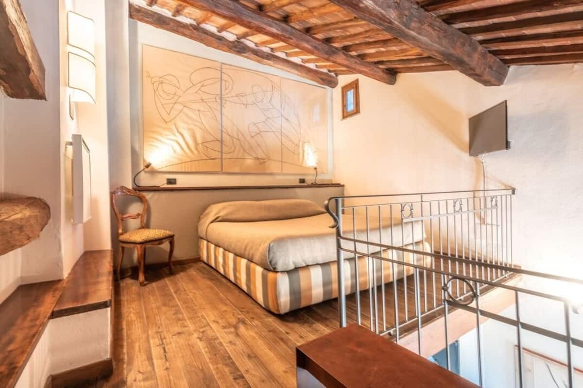 A cozy room with a wooden floor, a bed with striped bedding, a chair, and a large abstract painting on the wall.