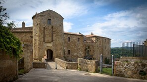 Explore a historic building with a central tower and smaller structures, set amidst stone walls and a metal gate.