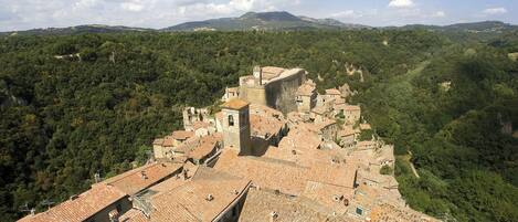 A historic town with terracotta-roofed buildings, a prominent tower, and a lush green valley in the background.