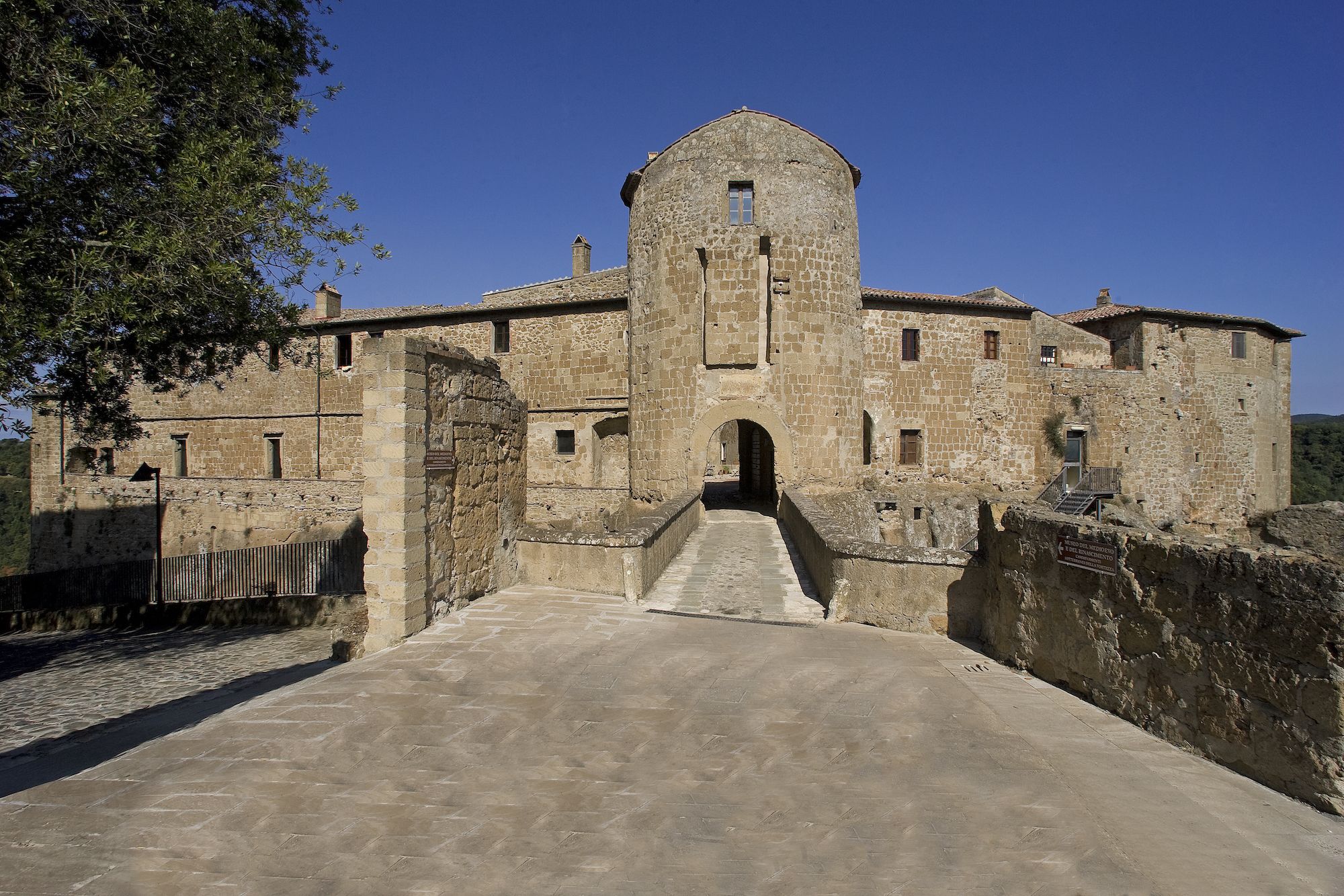 A historic stone building with a central tower, a paved entrance, and a surrounding wall.