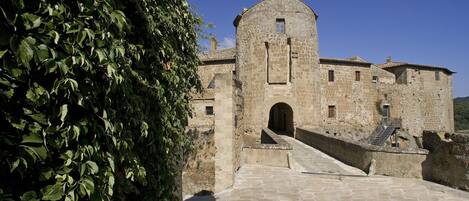 A historic stone building with a central tower, a covered entrance, and a paved courtyard.