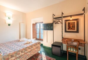 A bedroom with a bed, a desk, a chair, a radiator, and a window.