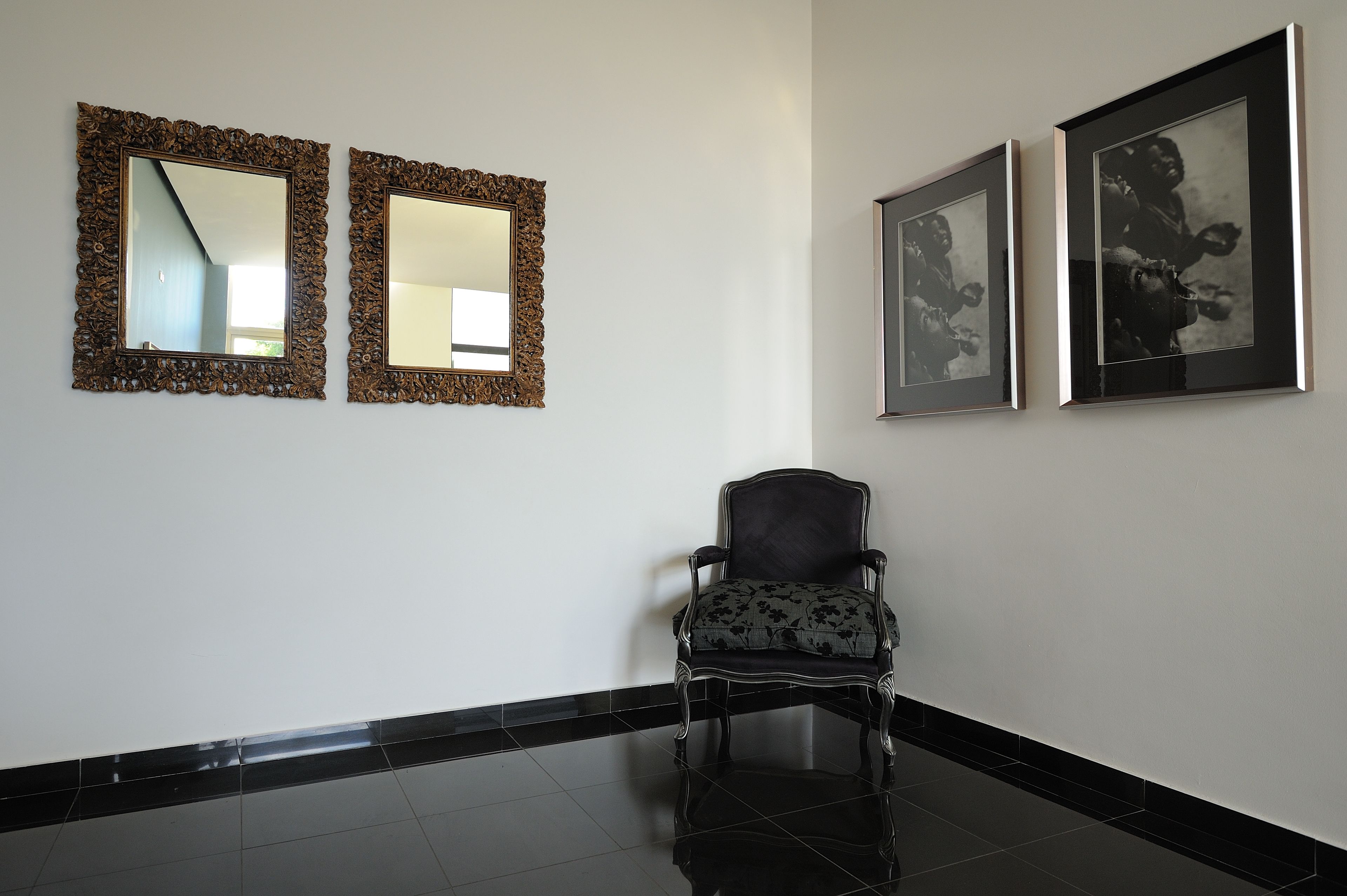 A room with two ornate mirrors, a framed photograph, and a chair.
