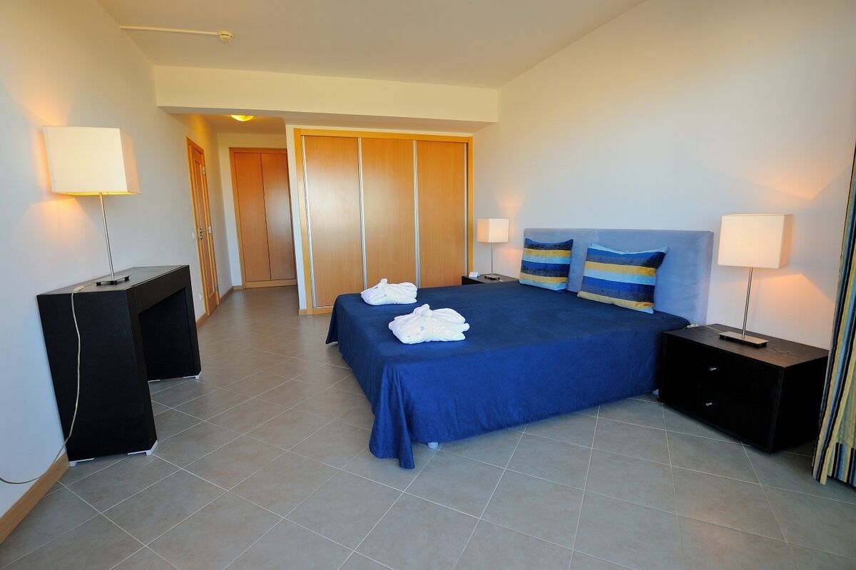 A hotel room with a bed, bedside tables, a desk, and a wardrobe.