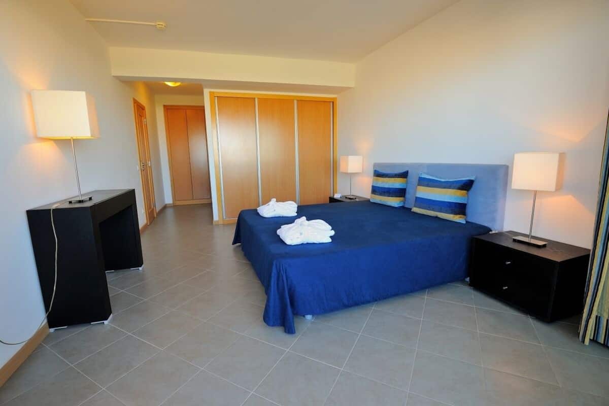 A hotel room with a bed, bedside tables, a desk, and a wardrobe.
