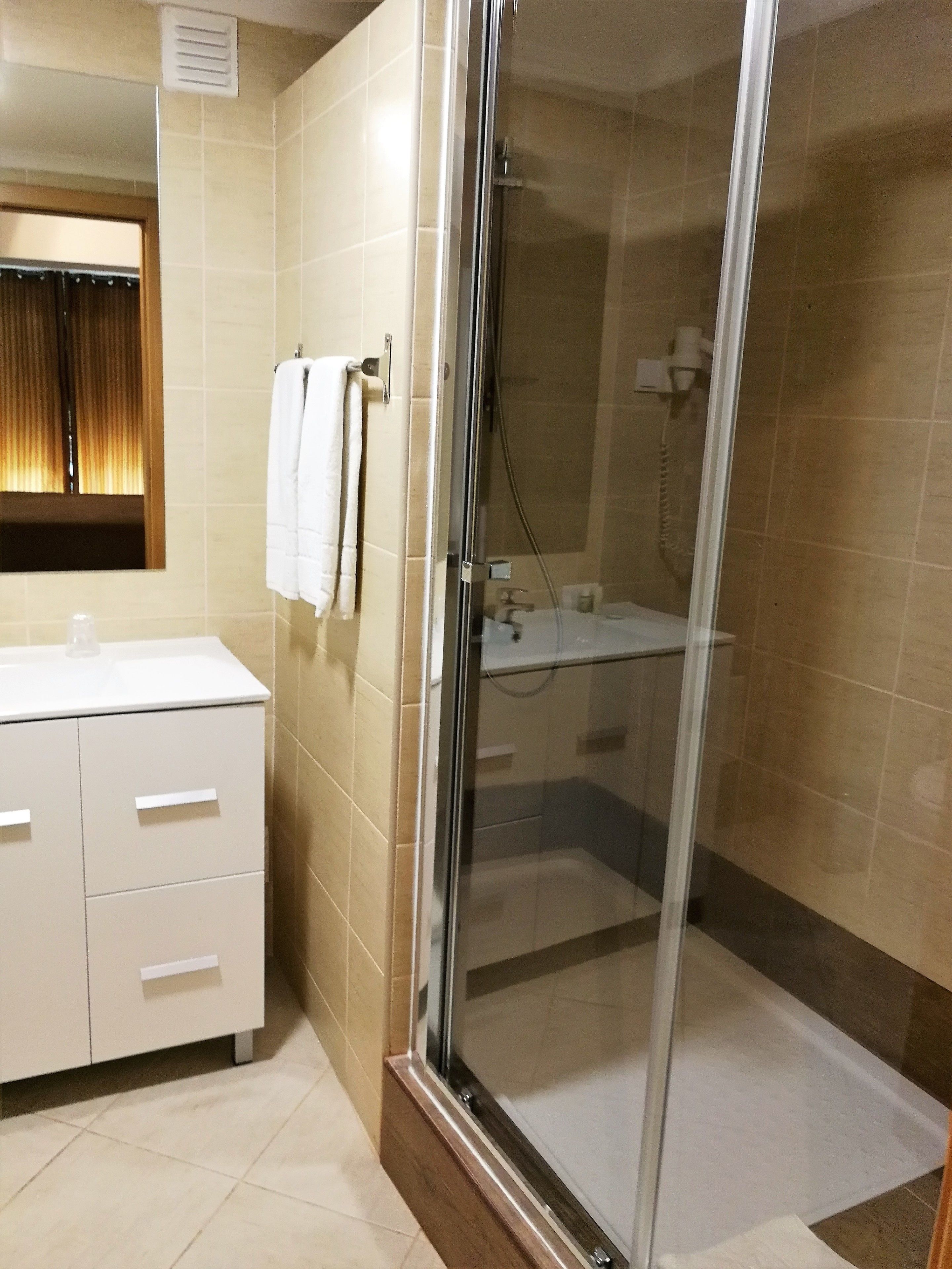 A modern bathroom with a glass-enclosed shower, a white sink, and a mirror with a curtain.