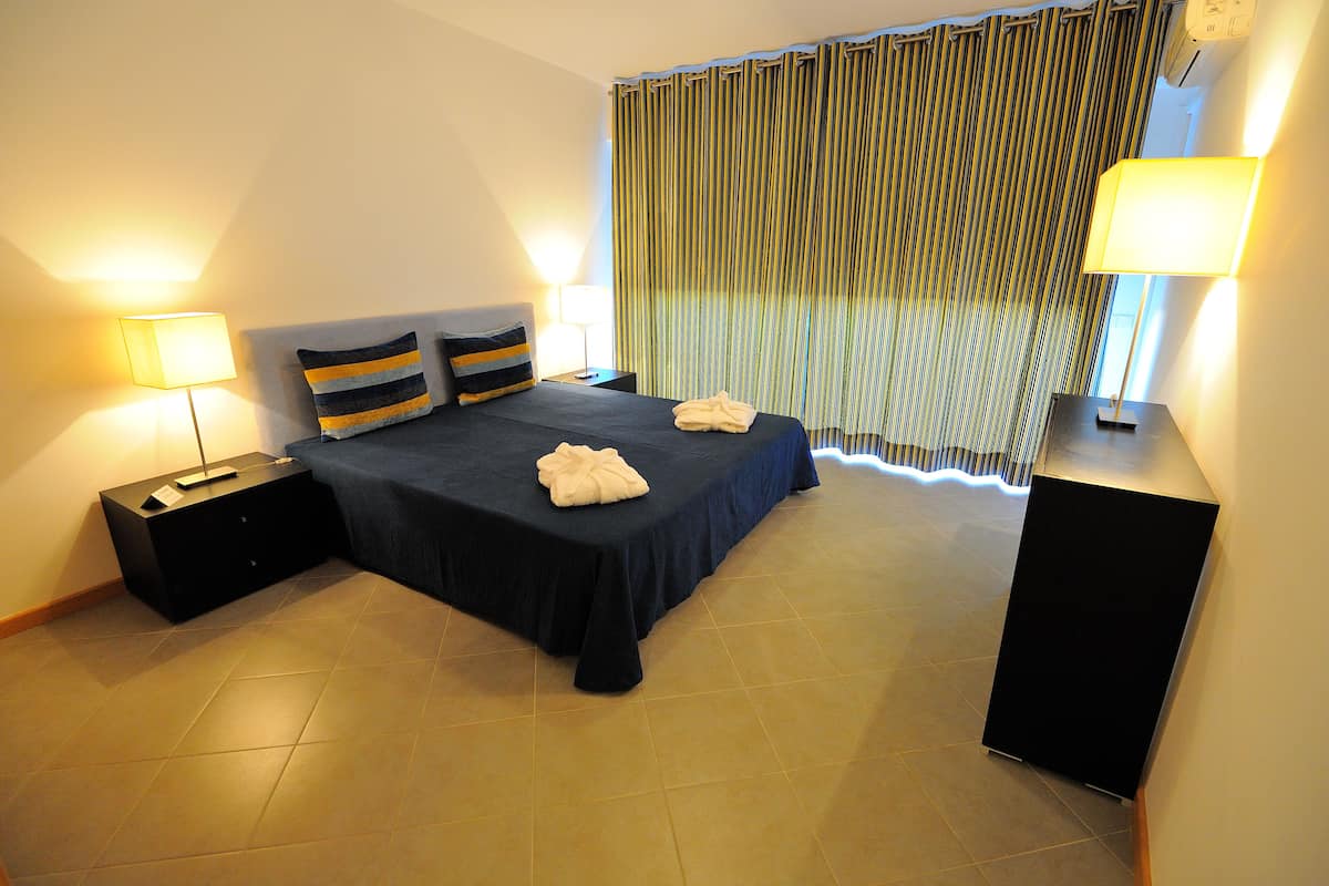 Una camera d'albergo con un letto, due comodini, una lampada, una tenda e un condizionatore d'aria a parete.