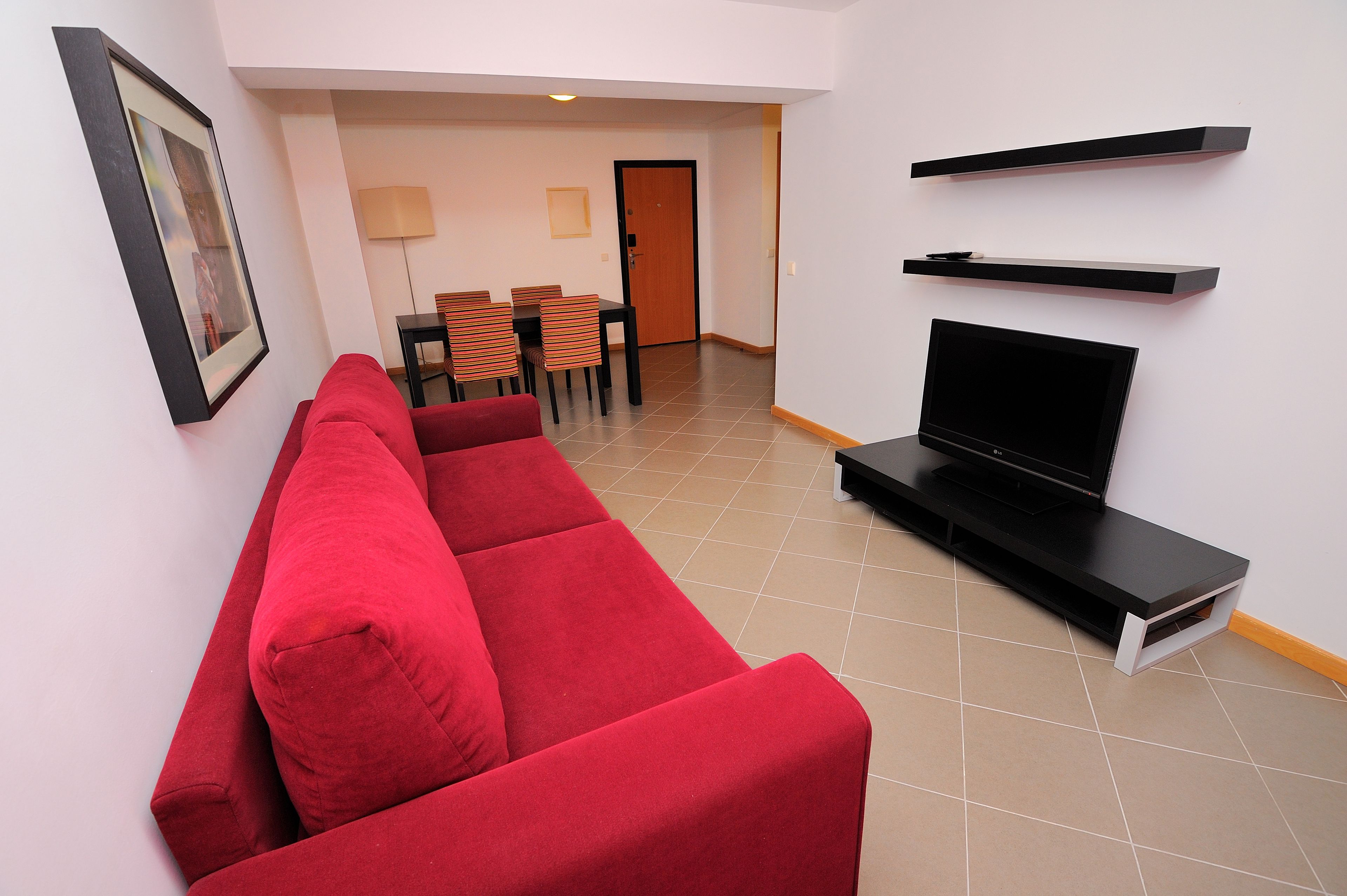 Una sala de estar con un sofá rojo, un televisor y un comedor con sillas y una mesa.