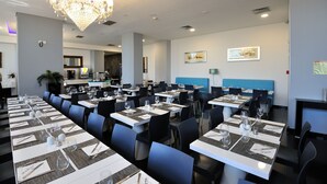 A modern dining area with tables set for service, a chandelier, and a blue booth seating area.