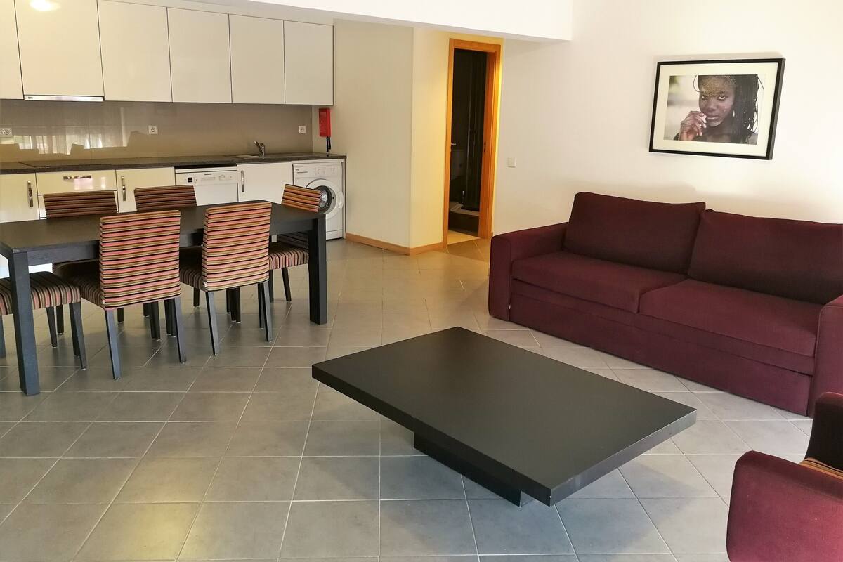 Un soggiorno moderno con un tavolino da caffè scuro, un divano rosso e sedie a righe disposte attorno a un tavolo da pranzo.