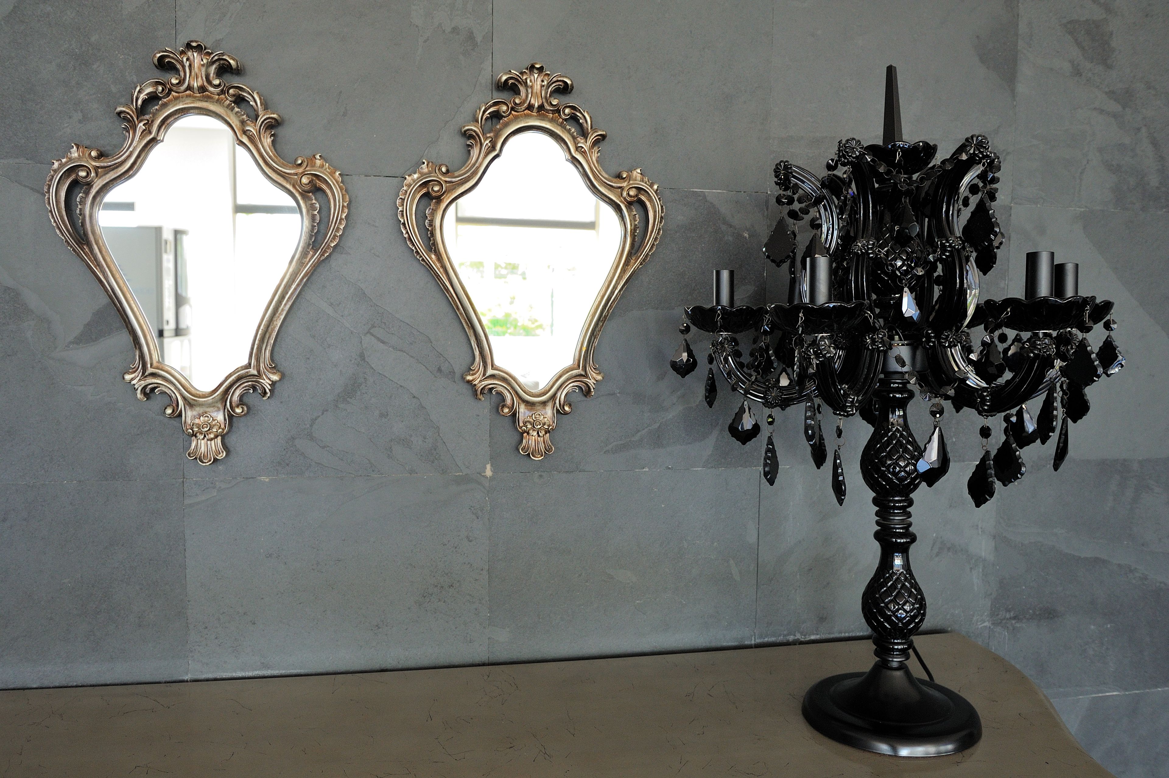 Two ornate mirrors and a black chandelier against a marble wall.