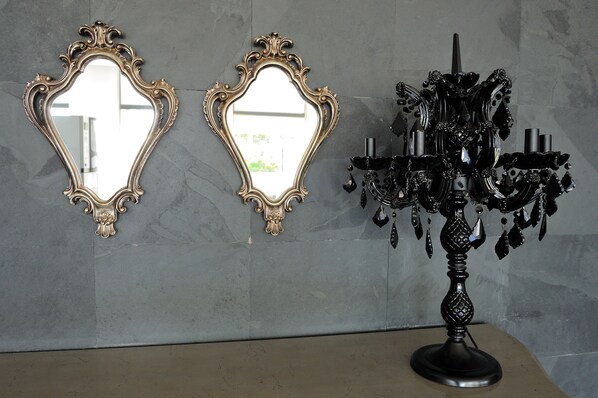 Two ornate mirrors and a black chandelier against a marble wall.