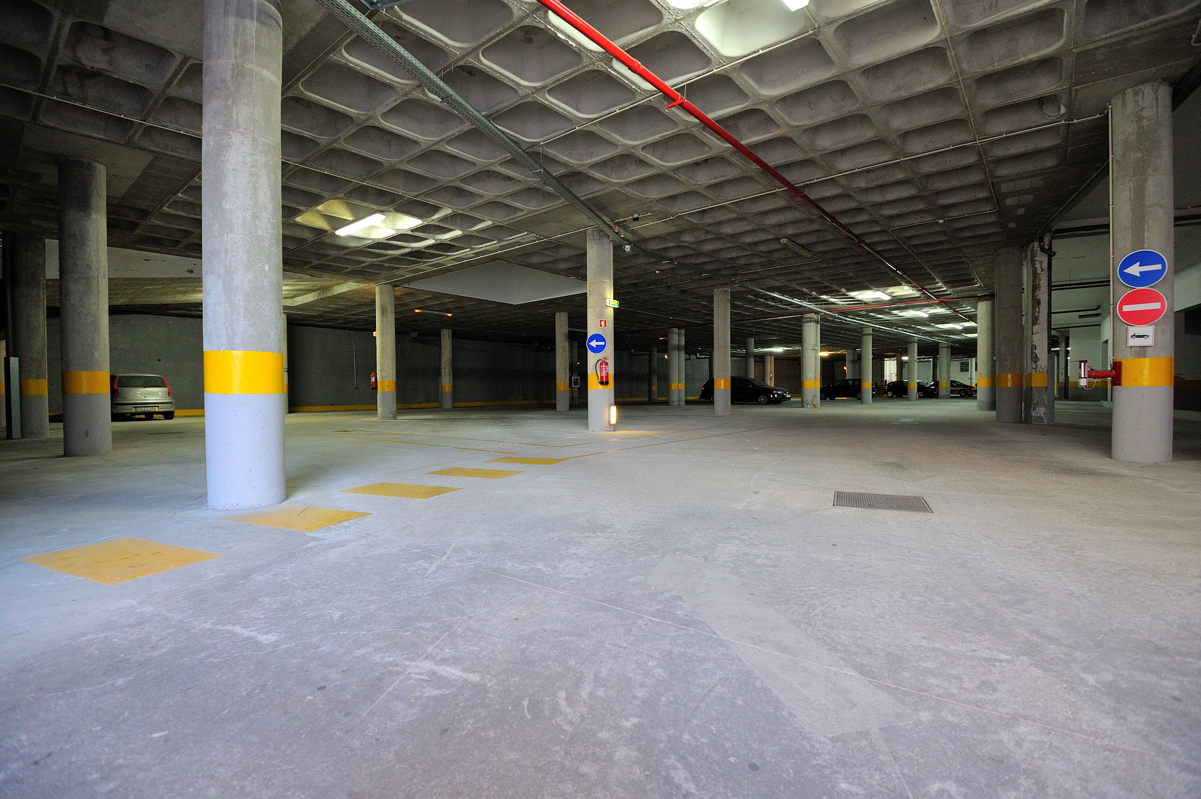 A multi-level parking garage with concrete pillars, yellow safety markings, and directional signs.